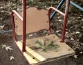 An unpaired children`s swing with a yellow back with iron red handrails an autumn leaf lies on the seat Royalty Free Stock Photo