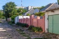 An unpaved street with a pink brick fence on the outskirts of a provincial town on a Sunny summer morning.