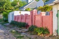 Unpaved street with a pink brick fence on the outskirts of a provincial town on a sunny summer morning.