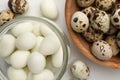 Unpeeled and peeled boiled quail eggs on white table