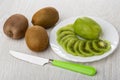 Unpeeled, peeled kiwi, slices of kiwi in plate, knife on wooden table