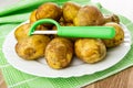 Unpeeled potatoes, peeler in plate on green napkin on wooden table