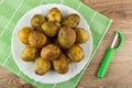 Unpeeled potatoes in plate on green napkin, peeler on table. Top view