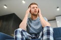 Unpleasant pain. Sad unhappy handsome man sitting on the sofa and holding his forehead while having headache. Royalty Free Stock Photo