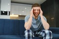 Unpleasant pain. Sad unhappy handsome man sitting on the sofa and holding his forehead while having headache. Royalty Free Stock Photo