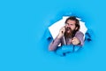 Unpleasant phone call. brutal bearded man shouting into telephone receiver. angry man torn blue background. male hipster