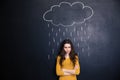 Unpleased woman with raincloud drawn over her on blackboard background