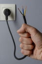 Unplug or plugged in concept, a hand holds an electrical cable plugged into an outlet