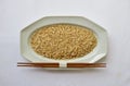 Unpolished brown rice on a white plate with chopsticks