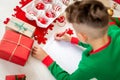 Unrecognisable boy wearing christmas pajamas writing letter to Santa on livingroom floor. Boy writing his christmas wishlist.