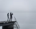 Unrecognisable people fishing in the fog on a pier or jetty. An unrecognisable guy is throwing the bait with a fishing rod