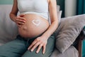 Unrecognisable pregnant woman with heart made of moisturiser on belly