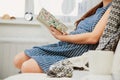Unrecognisable pregnant woman reading on sofa under gray plaid