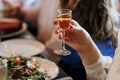 Unrecognisable woman holding glass of alcohol drink, cognac, liquor makes toast by the festive table, fun for a birthday