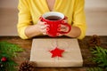 Unrecognisable woman sitting at a table with beautifully wrapped christmas present, holding cup of tea. Gift wrapping concept.