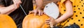 Unrecognisable young girl sitting on kitchen table, helping her father to carve large pumpkin. Halloween family banner.