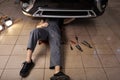 Unrecognizable auto mechanic lying and working under car