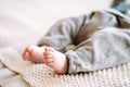 Unrecognizable barefoot infant newborn wearing grey bodysuit lying on beige cotton knitted plaid. Bedtime, maternity.