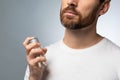 Unrecognizable bearded man spraying perfume on himself, using cologne for good smell, grey background, closeup Royalty Free Stock Photo