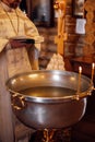 Unrecognizable bearded priest standing at font decorated with candles, reading prayer book during ceremony of baptism.