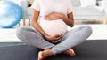 Unrecognizable black pregnant woman sitting in lotus pose on yoga mat and hugging her big tummy at home, panorama Royalty Free Stock Photo