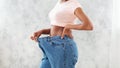 Unrecognizable black woman in oversized jeans showing results of her weight loss diet or liposuction, light background Royalty Free Stock Photo