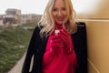 Unrecognizable blond ladylike woman warming with hot cup of coffee, looking at camera on cold balcony. Take away coffee