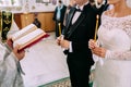 Unrecognizable bride and groom in the church during the Christian wedding ceremony. Hands of a priest with the Bible.