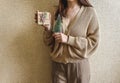 An unrecognizable brunette girl in a beige sweater holds a Christmas gift in eco packaging and a green Christmas tree in her hands Royalty Free Stock Photo