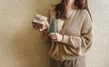 An unrecognizable brunette girl in a beige sweater holds a Christmas gift in eco packaging and a green Christmas tree in her hands Royalty Free Stock Photo