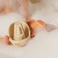 Unrecognizable child holding together cute beige and orange small silicone toy boats with holes on top in bubble bath. Royalty Free Stock Photo