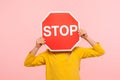 Unrecognizable child in yellow sweatshirt covering face with Stop symbol, anonymous person holding red traffic sign