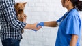 Unrecognizable client with cute little dog shaking hands with experienced veterinarian doc at clinic