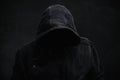 Unrecognizable cyber criminal or computer hacker wearing black hooded jacket, low key portrait