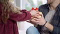 Unrecognizable daughter giving gift box to surprised father indoors. Little Caucasian girl and young man celebrating