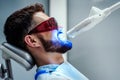 Unrecognizable dentist whitening teeth of young man sitting in dental chair in modern clinic. Side view