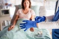 Unrecognizable doctor with patient in bed in hospital, putting on gloves.