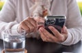 Unrecognizable elderly Caucasian woman sitting outdoors at cafe table in sunny day using mobile phone. Female hands holding Royalty Free Stock Photo