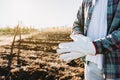 Unrecognizable farmer man wearing gardening gloves in the middle of the farmland. Agricultural sustainability concept.