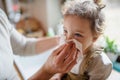 Unrecognizable father blowing nose of small sick daughter indoors at home.