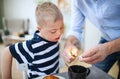 Unrecognizable father with down syndrome son indoors, lighting candle. Royalty Free Stock Photo