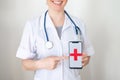 Unrecognizable female doctor holds a smartphone with a red cross on the screen. The nurse smiles and points to the