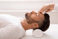 Massage therapist rubbing relaxed man forehead, spa interior Royalty Free Stock Photo