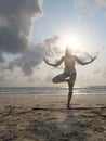 Unrecognizable female practicing balancing yoga asana at sandy beach in sun shine. Vertical photo