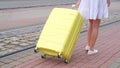 An unrecognizable female traveler walks along the street near the tram tracks with a yellow suitcase Royalty Free Stock Photo