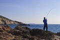 Unrecognizable fisherman a man stands on the sea shore with rocks and pulls the rod, biting the fish.