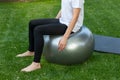 Unrecognizable fitness slim man sitting on a balace ball while exercising barefoot in the garden fresh grass