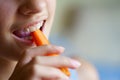 Unrecognizable girl eating fresh carrot slice at home