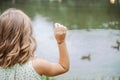 Unrecognizable girl in light dress stands with her back and feeds ducks near pond in nature. Royalty Free Stock Photo