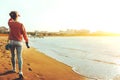 Unrecognizable Hiker Girl In Jeans Walks Along The Seashore With Binoculars, Rear View. Scout Wanderlust Holidays Concept